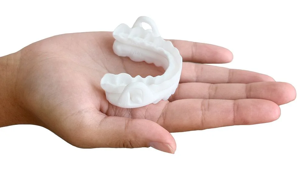 Photo of a mandibular advancement device (MAD) on a dental model: two splints connected by an advancement mechanism, used to reduce snoring and mild to moderate sleep apnea.