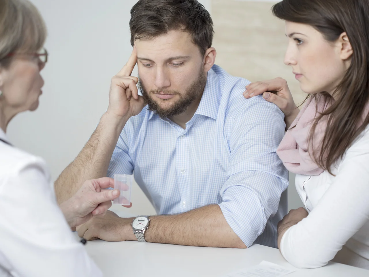 Couple at a fertility consultation with a doctor holding a sample container.